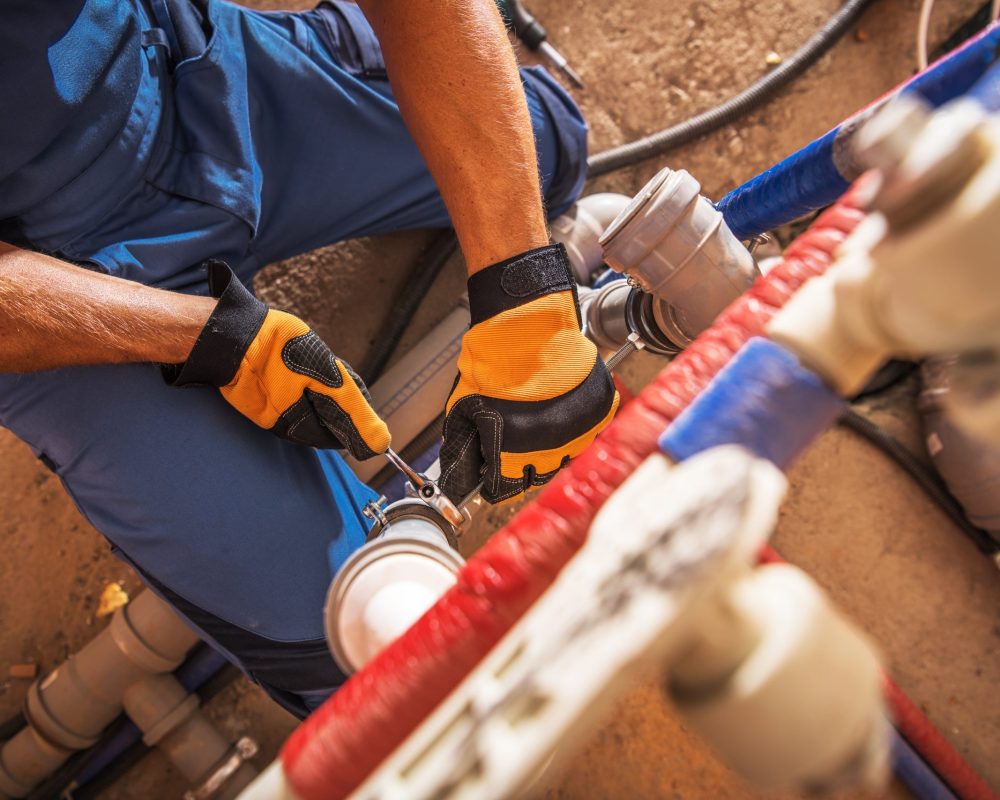 A plumber uses tools to fix piping systems in a construction setting, showcasing hands-on work and problem-solving skills in plumbing repairs.