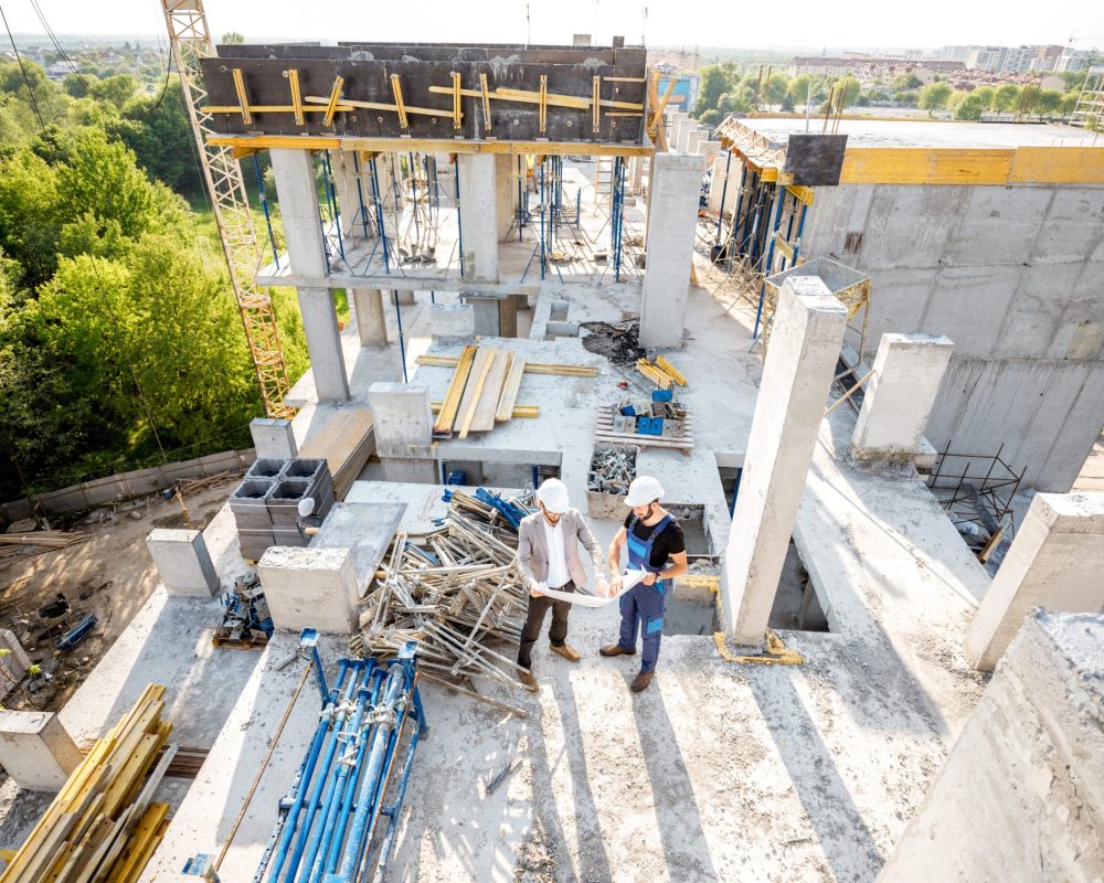 Top view on the construction site of residential buildings during the construction process with two workers standing with drawings